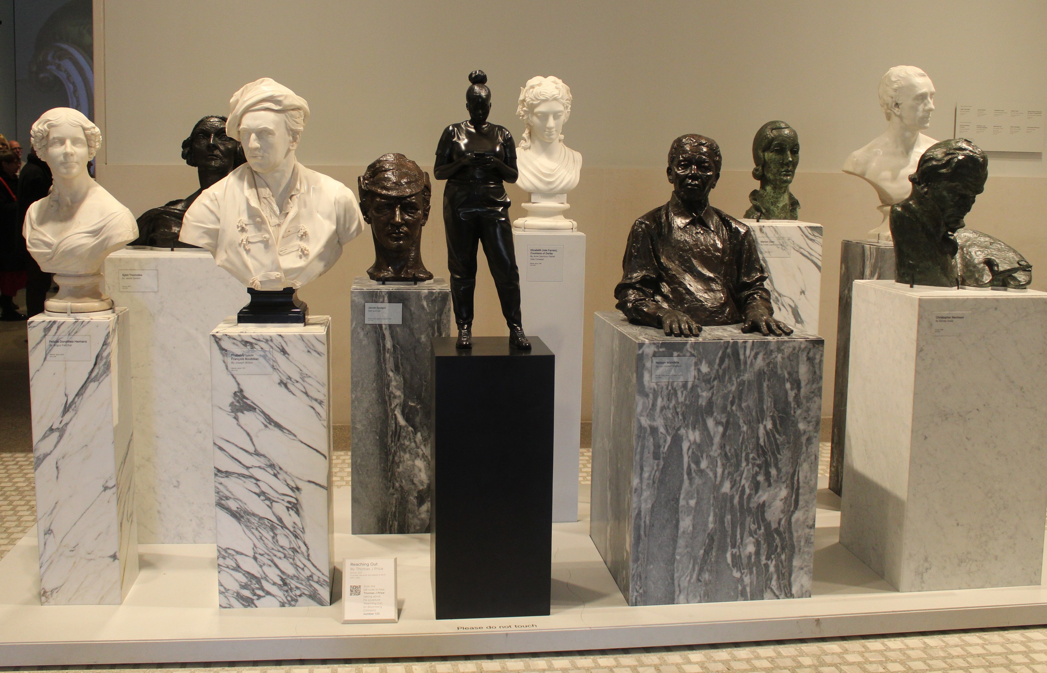 Gruppe von lebensechten Büsten-Skulpturen in einem Museum ausgestellt, mit Besuchern im Hintergrund und einer Wand dahinter.