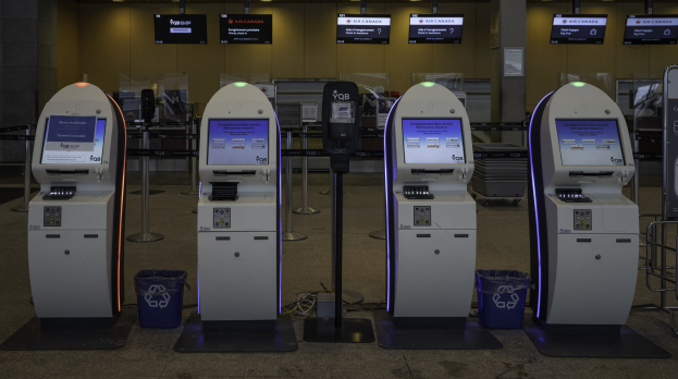 Eine Reihe von Geldautomaten auf einem gefliesten Boden mit Mülltonnen, Pfosten, Texttafeln, Lampen und anderen Gegenständen im Hintergrund.