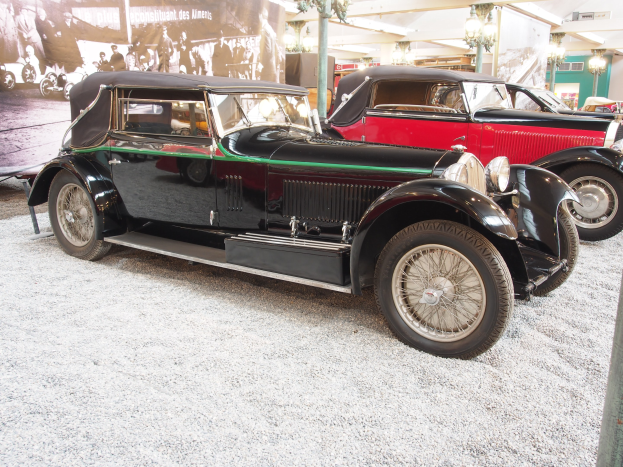 Eine Gruppe von Oldtimern in einem Museum ausgestellt, mit einem Banner auf der linken Seite, das Bilder von Menschen und Text zeigt, unter Deckenleuchten, die eine gemütliche Atmosphäre schaffen.