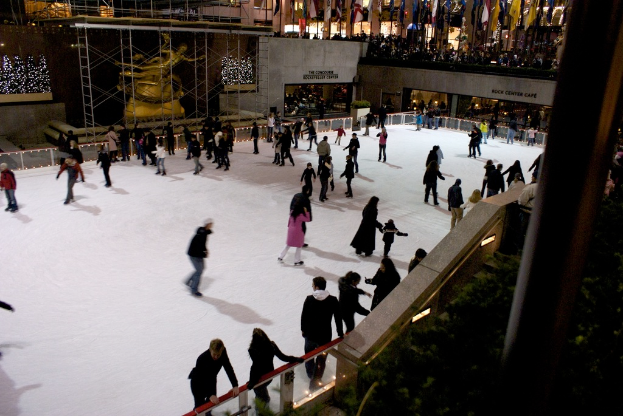 Eine große Gruppe von Menschen, die auf einer zugefrorenen Fläche Schlittschuh laufen, umgeben von Gebäuden.