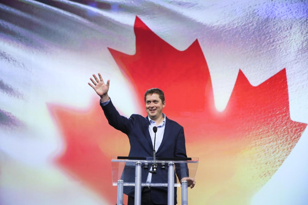 Der kanadische Premierminister Alex Salmond steht an einem Podium mit Mikrofonen, strahlend vor einer kanadischen Flagge, mit einem sichtbaren Bildschirm im Hintergrund.