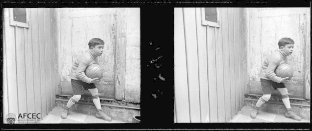 Ein junger Junge steht vor einer hölzernen Tür und hält einen Fußball in den Händen, dargestellt in Schwarz-Weiß.