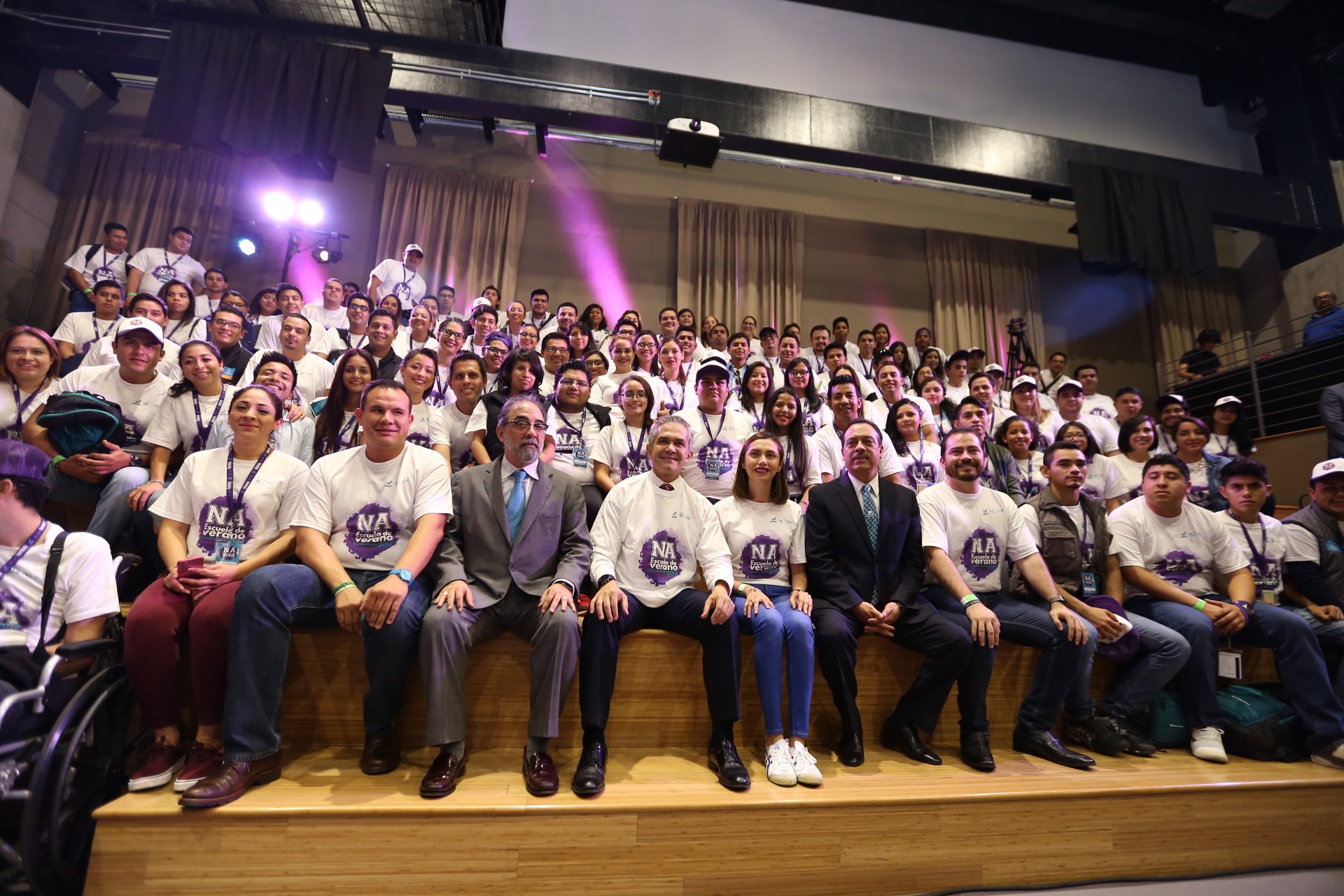 Eine Gruppe von Menschen auf einer Bühne mit einer Person im Rollstuhl links, vor einem Vorhang, Scheinwerfern und einer Wand auf der Nationalen Konferenz der Frauenbasketball-Vereinigung.