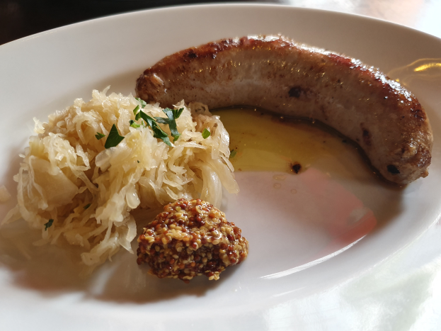 Ein weißer Teller mit Sauerkraut, deutscher Wurst und anderen Speisen, gezeigt in einer Nahaufnahme auf einem Tisch.