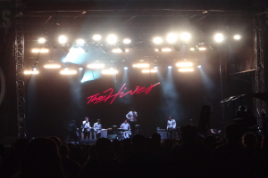 Eine Gruppe von Musikern, die auf der Bühne mit Instrumenten spielen und ein Sänger mit Mikrofon, während das Publikum unten zuschaut.