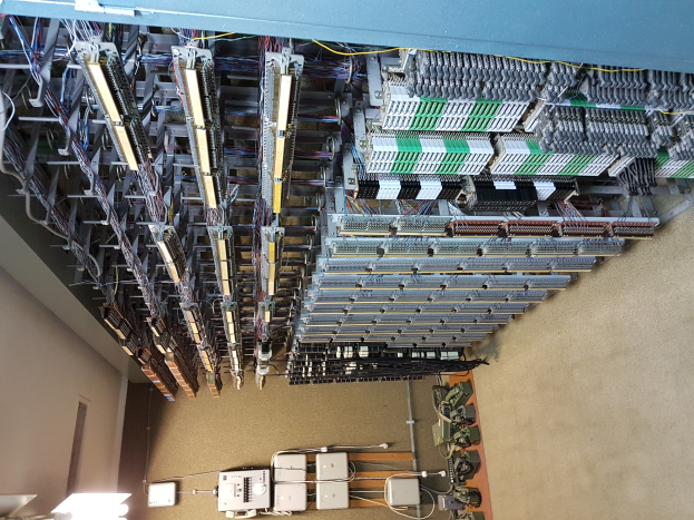 Ein großer Raum voller numerous wires und elektronischen Geräten auf dem Boden, mit einer Wand auf der linken Seite, der einem Datenzentrum mit verschiedenen Servern und interconnected cables ähnelt.