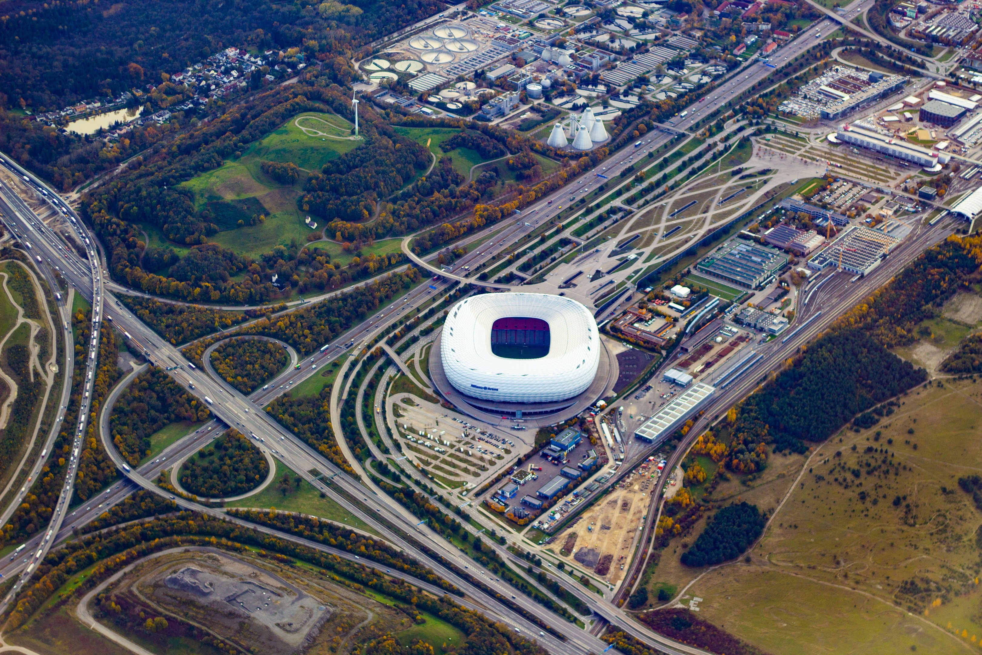 Luftaufnahme des Olympiastadions in München, Deutschland, umgeben von Gebäuden, Bäumen, Stra√en, Fahrzeugen und Gras.