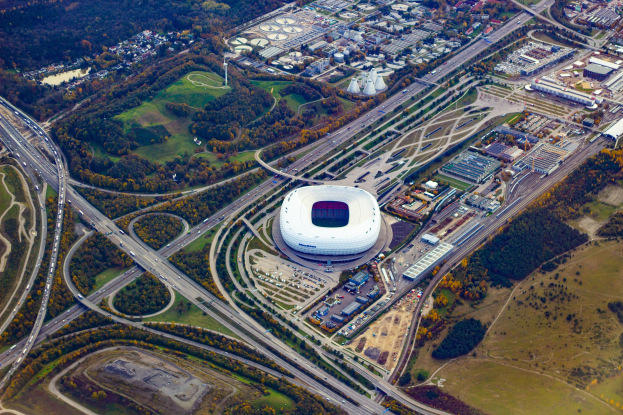 Luftaufnahme des Olympiastadions in München, Deutschland, umgeben von Gebäuden, Bäumen, Stra√en, Fahrzeugen und Gras.