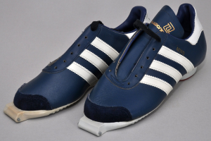 Ein Paar blaue und weiße Adidas Originals Samba OG-Schuhe mit weißen Schnürsenkeln und einer weißen Zwischensohle und Außensohle, die auf einer grauen Oberfläche präsentiert werden.