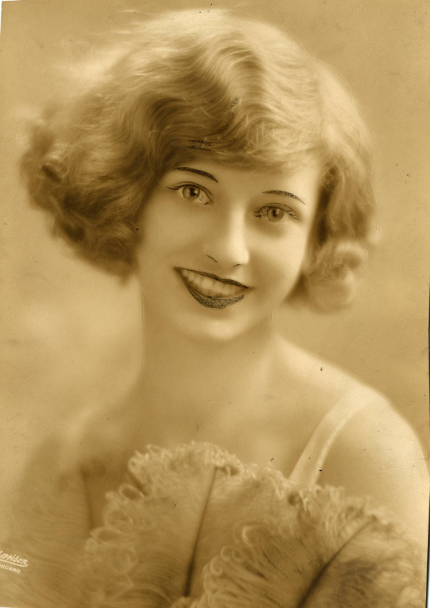 Ein Schwarz-Weiß-Foto einer Frau in einem Kleid im Stil der 1920er Jahre mit einem klassischen Bob und einem warmen Lächeln.