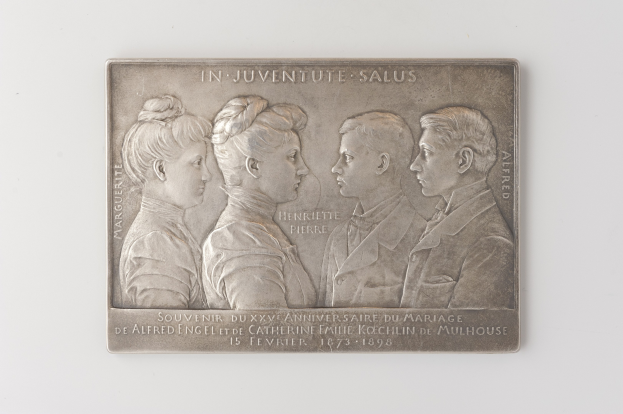 Silberne Plakette mit drei Personenbildnissen und eingraviertem Text, wahrscheinlich eine Heiratsgedächtnis, auf einem weißen Hintergrund.