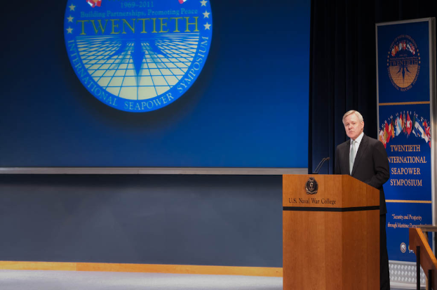 US-Außenminister Mike Pompeo trägt einen schwarzen Blazer, ein weißes Hemd und eine schwarze Krawatte und steht an einem Podium mit zwei Mikrofonen vor einem blauen Hintergrund bei der 20. Internationalen Seemacht-Symposium, mit einem Geländer rechts daneben.