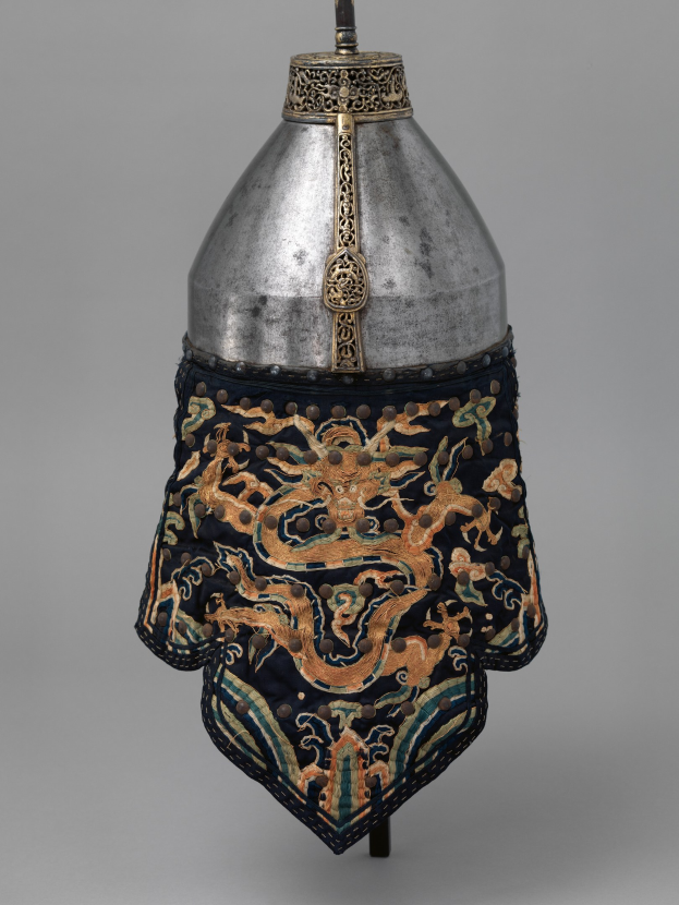 Metallhelm mit Drachendesign vor einem grauen Hintergrund.