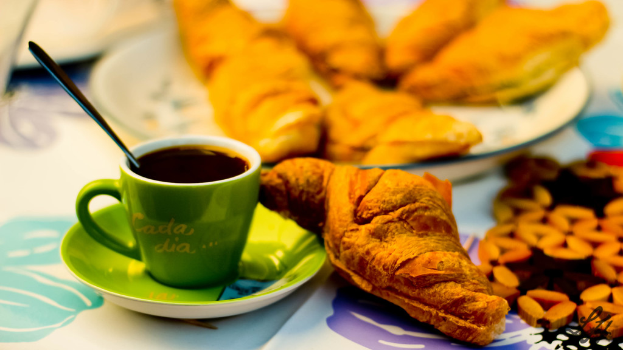 Ein Tisch mit einer Decke, auf der eine Teetasse, Untertasse, Löffel und ein Teller mit Speisen stehen.