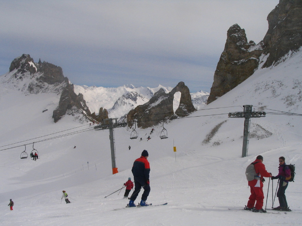 Menschen in Pullovern fahren Ski, mit Seilbahn, Bergen und bewölktem Himmel im Hintergrund.