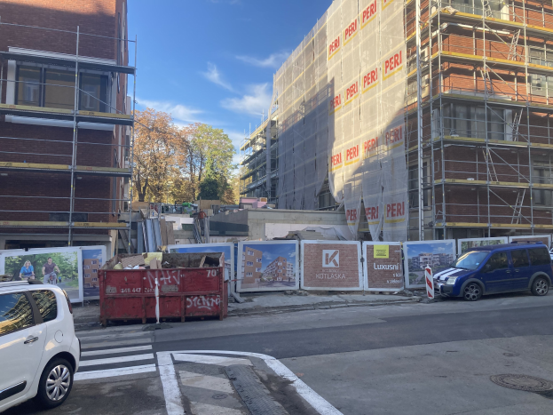 Stadtstraße mit parkenden Autos, Gebäuden, Bäumen und einem bewölkten Himmel, mit verstreuten Tafeln mit Text und Bildern.