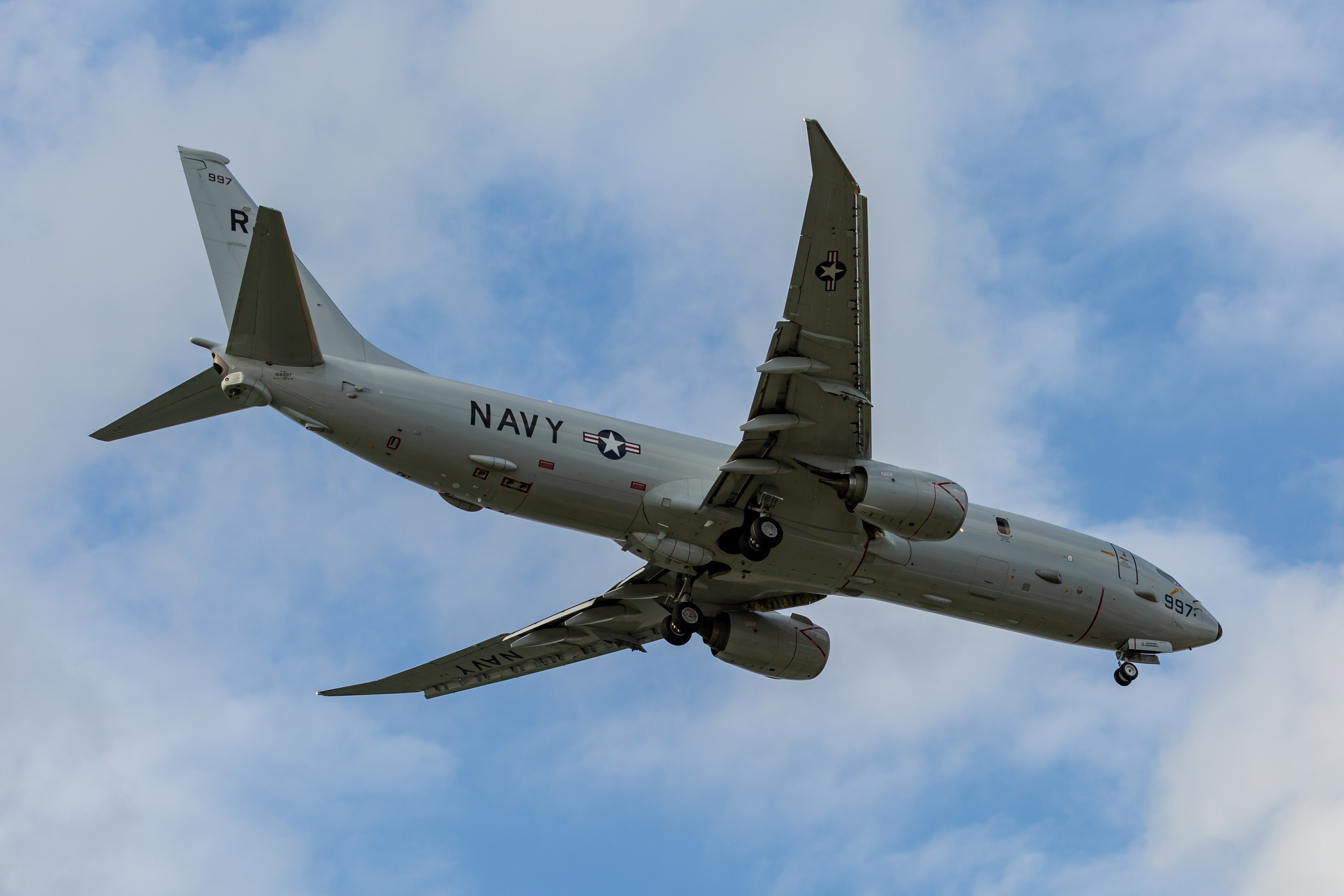 Ein großes Militärflugzeug fliegt in einem blauen Himmel mit weißen Wolken, das mit Text und Zahlen gekennzeichnet ist, die darauf hinweisen, dass es eine Joint Direct Attack Munition ist.