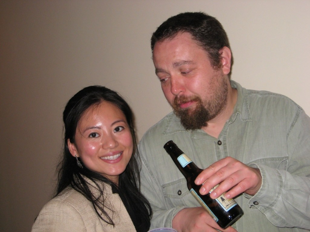 Ein Mann mit einer Flasche starrt eine lachende Frau vor einer Wand an.