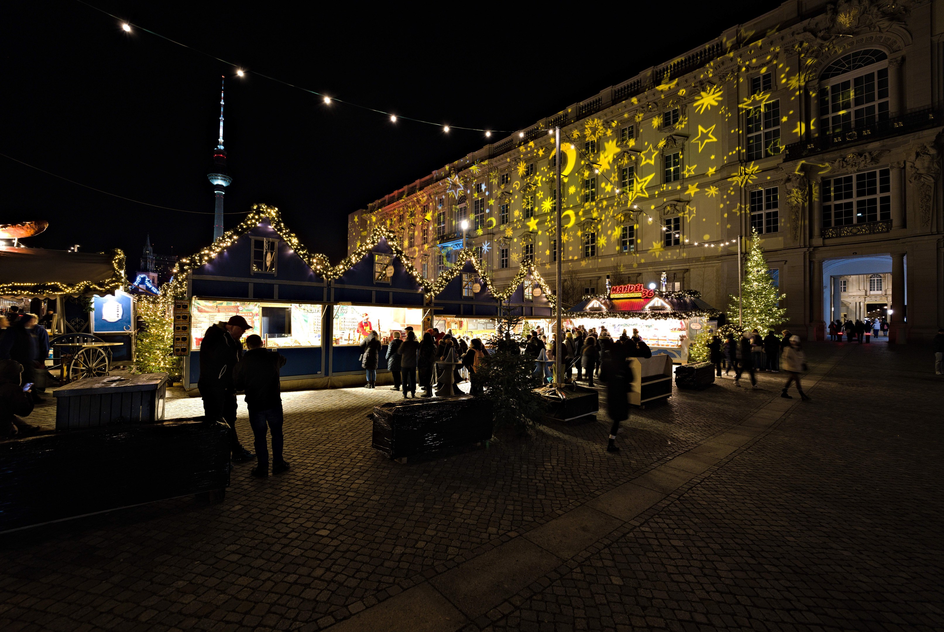 Ein geschäftiger Weihnachtsmarkt in Berlin, Deutschland mit Menschen, die sich um geschmückte Stände, festliche Lichter und dunklen Himmel versammeln.