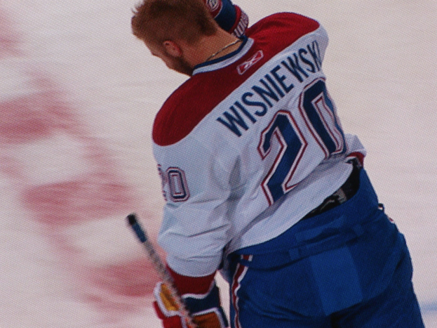 Professional hockey player wearing a "Wisniewski" jersey, gripping a hockey stick on ice with a focused expression.