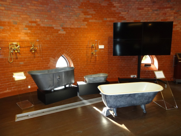 Ein gemütliches Badezimmer mit einer Backsteinwand, einer zentralen Wanne, an der Wand montierten Wasserhähnen auf der linken Seite und einem an der Wand montierten Fernseher auf der rechten Seite.