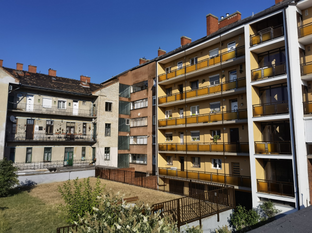 Wohngebäude mit Innenhof und Grünfläche, Pflanzen, Bäumen und sichtbarem Himmel im Hintergrund.