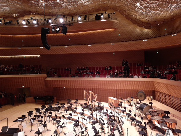 Großer Auditorium mit Musikinstrumenten, Stühlen, Ständern mit Papieren und Menschen, mit beleuchteter Decke, im Berliner Philharmoniker.