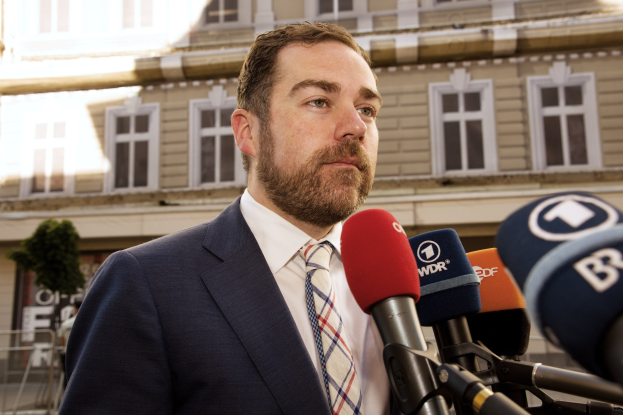 Ein Mann im Anzug spricht vor einem Gebäude mit der Medien, wahrscheinlich wegen einer dreijährigen Haftstrafe.