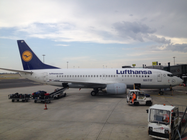 Lufthansa Airbus A320-200 auf dem Frankfurt Airport geparkt mit Bodenfahrzeugen, Verkehrskegeln und Beschilderung im Hintergrund unter einem bewölkten Himmel.