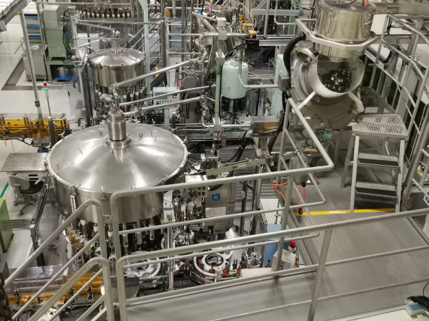 Ein großes Reaktorgerät in einem Gebäude umgeben von verschiedenen Komponenten und Maschinen, mit einem Boden, Geländern und Treppen.