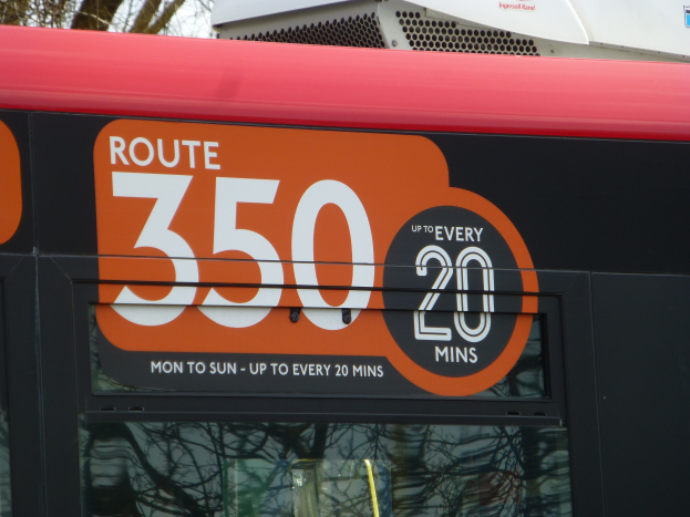 Roter Doppeldeckerbus mit der Aufschrift "Route 350", der durch einen baumbestandenen Bereich unter einem klaren Himmel fährt.