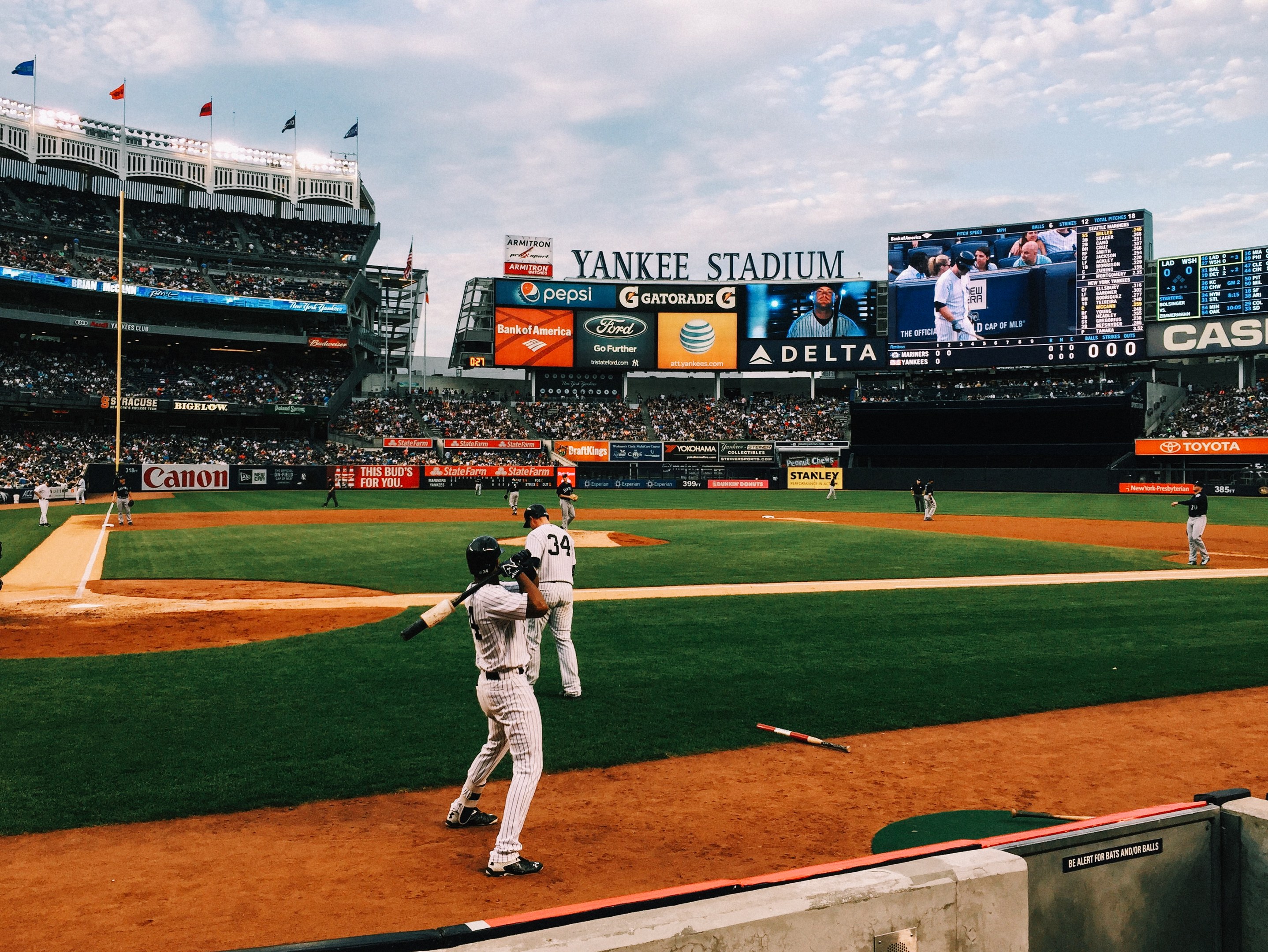 Baseballspiel im Gange im Yankee Stadium mit Spielern auf dem Feld und Zuschauern in den Röngen unter einem bewölktem Himmel.