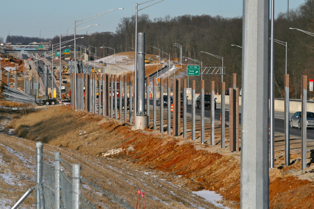 Baustelle mit Fahrzeugen, Polen, beleuchteten Schildern, einem Zaun, schneebedeckter Wiese, Bäumen und einem Himmel im Hintergrund.