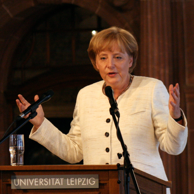 Bundeskanzlerin Angela Merkel hält eine Rede an der Universität Leipzig und steht vor einem Rednerpult mit einem Mikrofon und einem Glas Wasser.