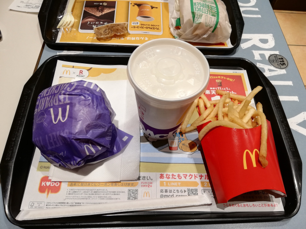 Ein Tisch mit einem Tablett, das ein McDonald's-Essen einschließlich Pommes, einen Kaffee, ein Papier, eine Gabel und ein Messer enthält.