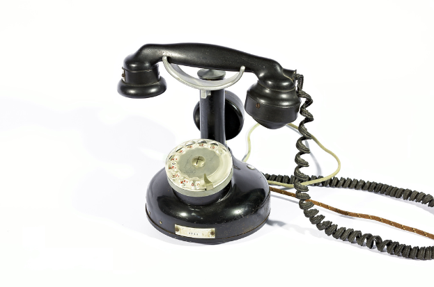 Ein schwarzes Telefon mit Zahlen und Text, der durch die Glasscheibe sichtbar ist, verbunden durch Drähte, vor einem weißen Hintergrund.