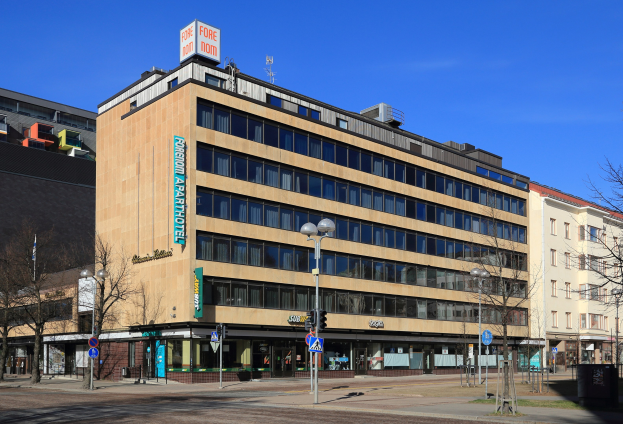 Großes Gebäude mit zahlreichen Fenstern, identifiziert als das Fore Inn Hotel Berlin, umgeben von Straßeninfrastruktur einschließlich Pfosten, Lampen, Signalen, Schildern, Bäumen und einem bewölkten Himmel.
