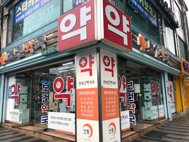 Ein Gebäude mit Glaswänden und -türen, das Schilder trägt, die "Südkoreas erste Apotheke in Seoul, Südkorea" lesen, und ein Schild an der Seite.